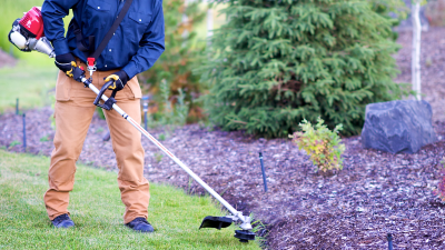 Wide, waist-down view of a gardener trimming the edge of a lawn. 