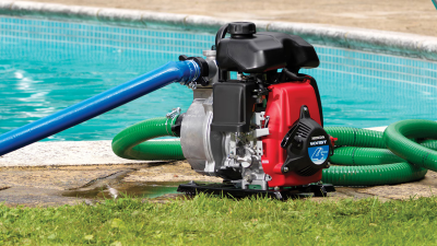Wide view of portable transfer pump, with hoses plugged in, sitting next to residential pool.