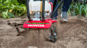 Head-on view of gardener pushing tiller through very dry and dusty soil.  